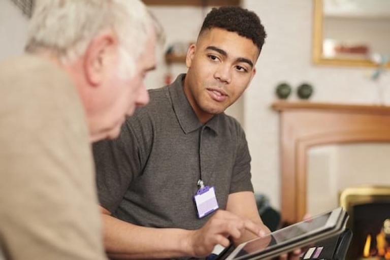 Young care worker sitting with elderly male client